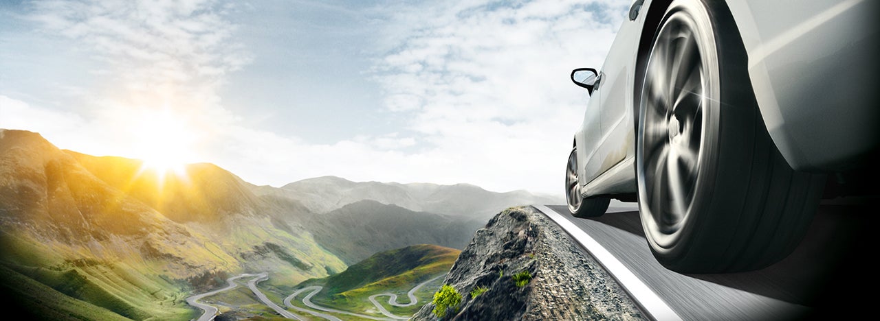 Car driving on a mountain with a sunny valley in background.