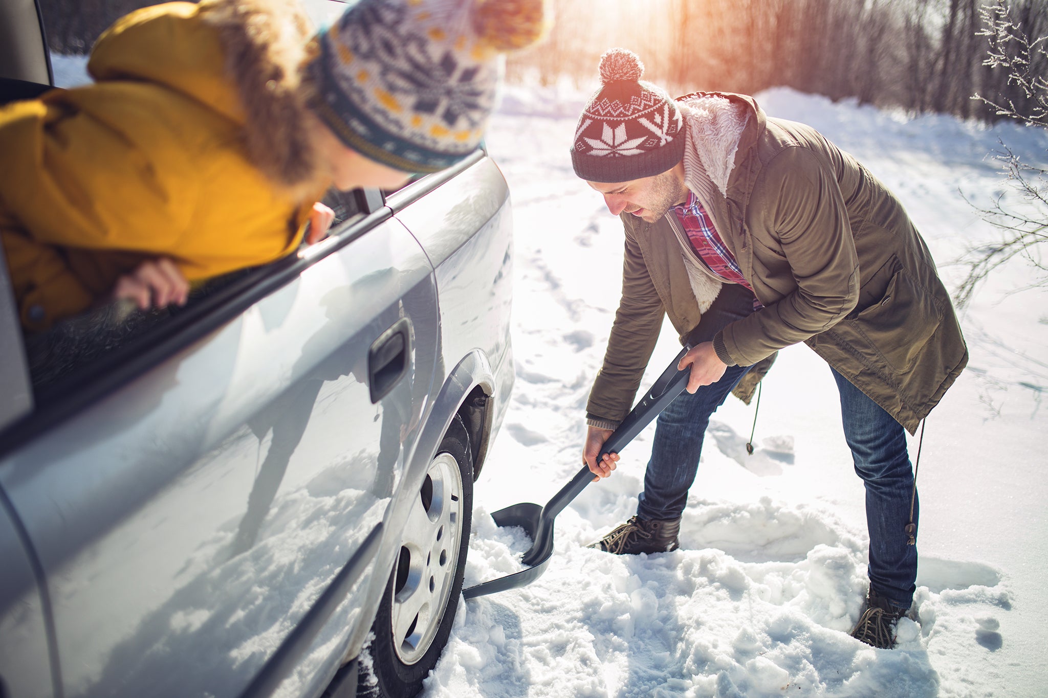 A man cleans snow near the car with shovel in nature.