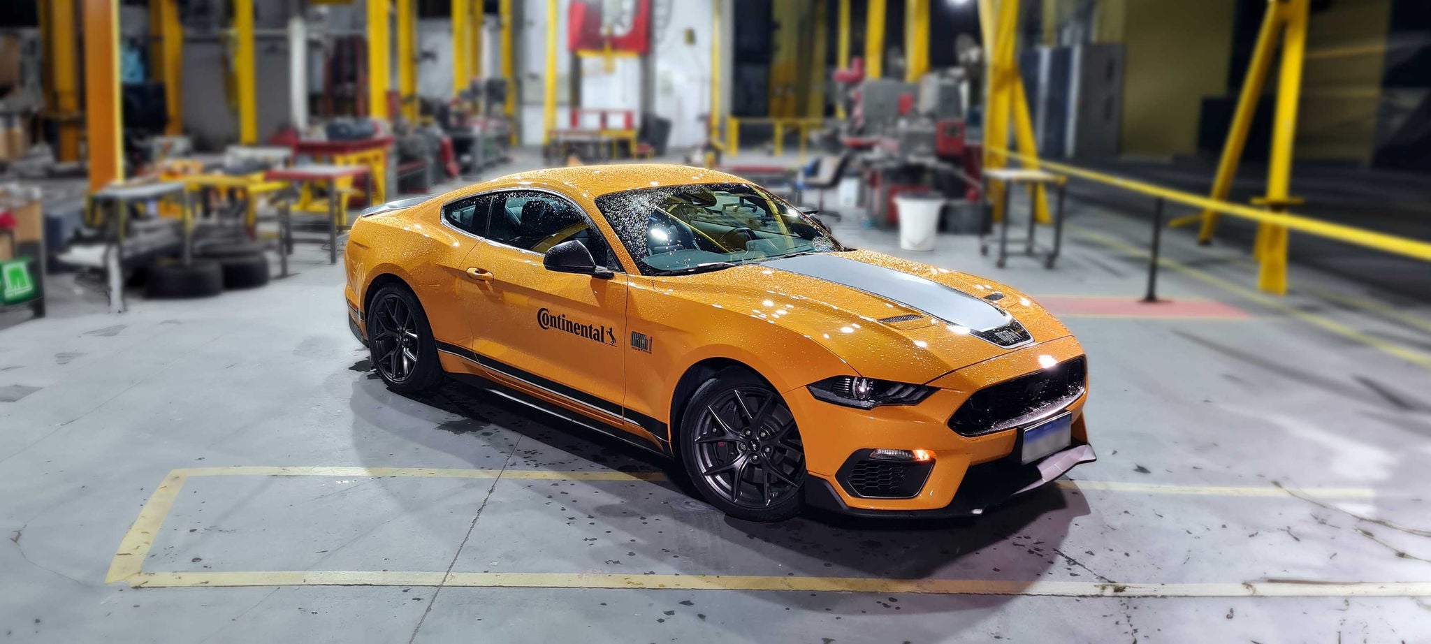 (imagem de carro esportivo V8 amarelo Continental com adesivo Continental em ambiente de teste industrial)