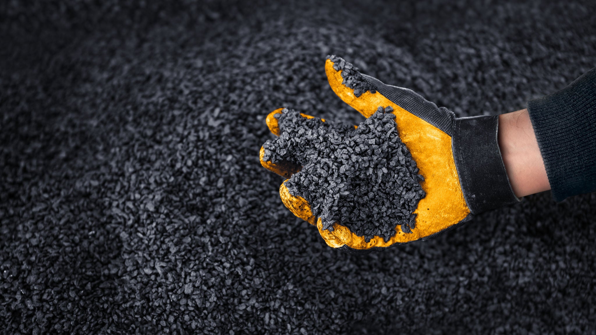 A hand with safety glove reaches into remnants of scrap tires